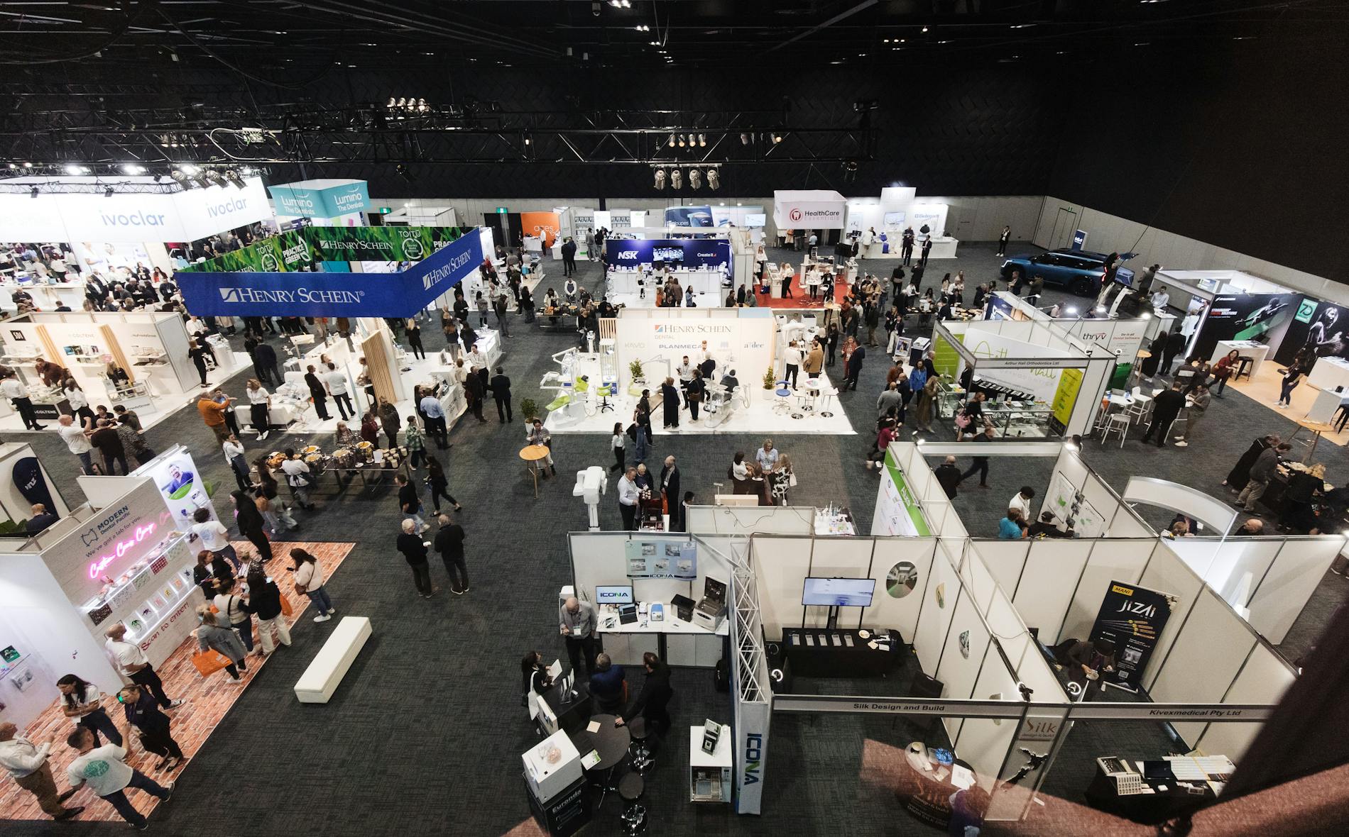 A bustling trade show features numerous branded booths, including 'Te Pae.' Attendees engage with displays and products in a spacious, modern exhibition hall, fostering networking and exploration.
